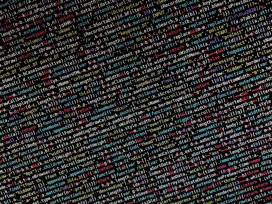 A photograph of a computer screen displaying dense computer code with multicolored lines of HTML, CSS, and JavaScript syntax. The code features functions, variables, and commands highlighted in variou