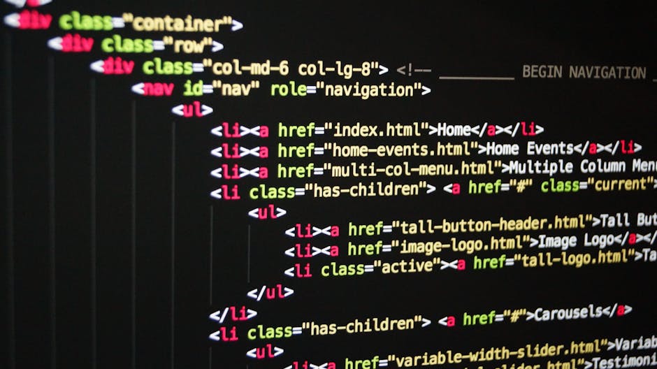 Close-up of a person's hands typing on a laptop located on a dark table, with code displayed on the screen in a dark-themed text editor, featuring lines of coloured syntax. The laptop is surrounded by