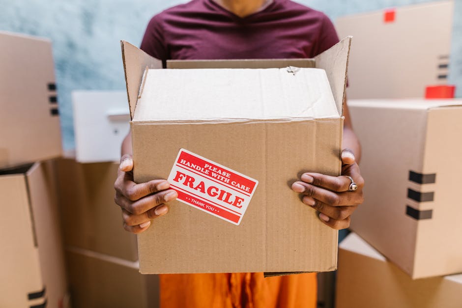 A professional mover from Barnes Storage is carefully lifting a green upholstered sofa, positioned vertically with the backrest facing outward, through a doorway into a room with a wooden paneled wall