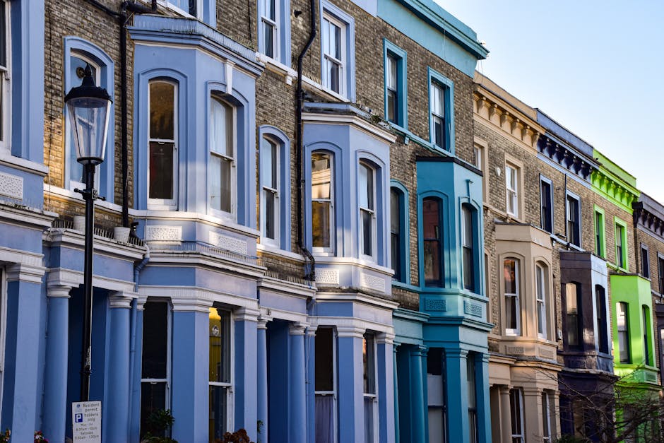 Photograph of a row of Victorian terraced houses on Barnes High Street, featuring red brick facades with white decorative architectural details around the multi-pane sash windows and entryways. Black 